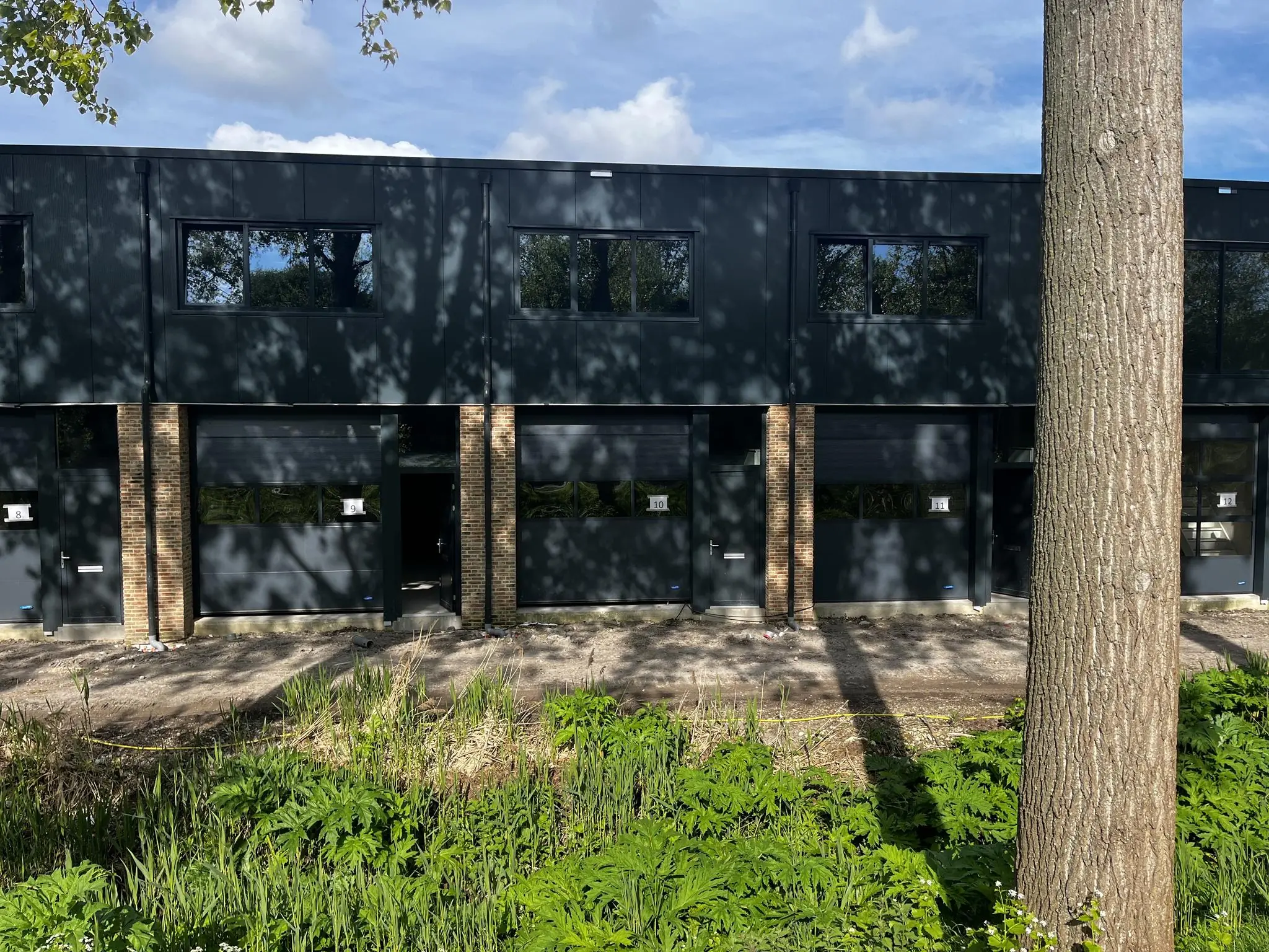 Moderne bedrijfsunits aan de Broekdijk West met zwarte gevels en grote ramen, omringd door groen.